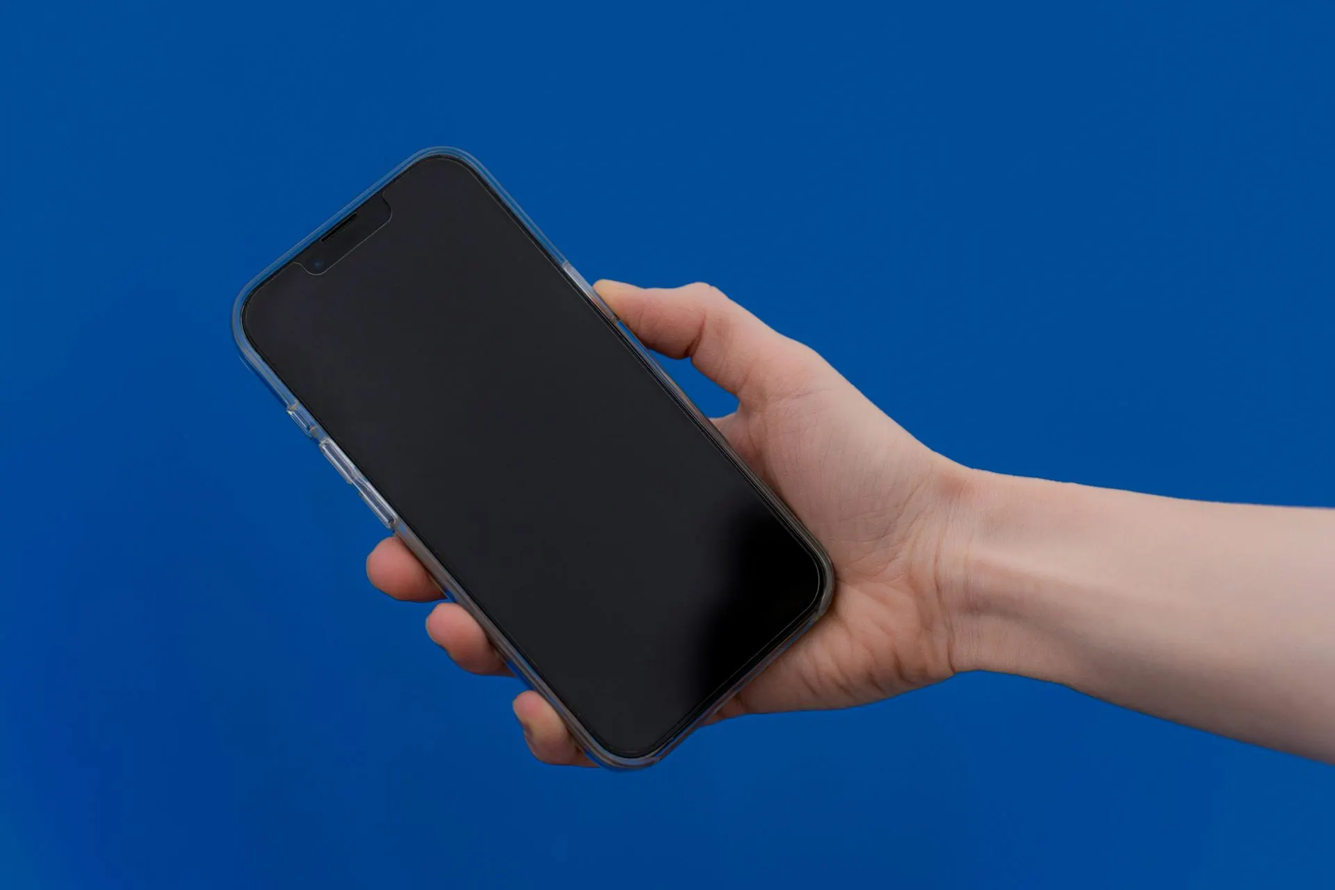 Eine Hand hält ein schwarzes Smartphone vor blauem Hintergrund.