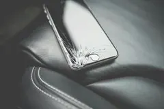 Ein gesprungener Smartphone-Bildschirm liegt auf einer schwarzen Lederoberfläche.