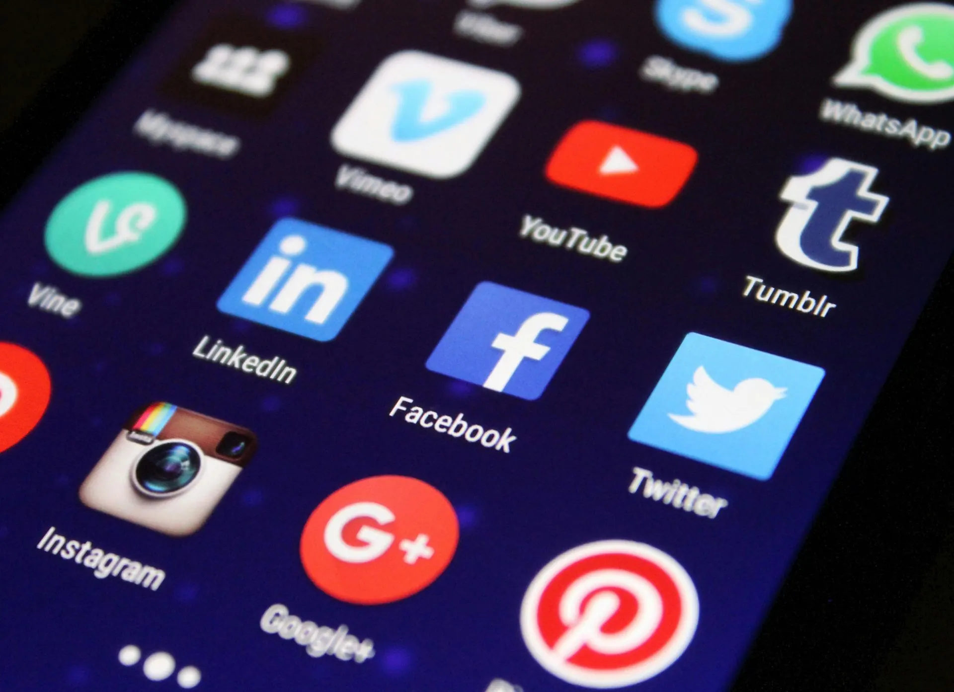 Smartphone-Bildschirm mit Symbolen für Social-Media-Apps, darunter Facebook, Instagram, Twitter und YouTube, auf dunkelblauem Hintergrund.