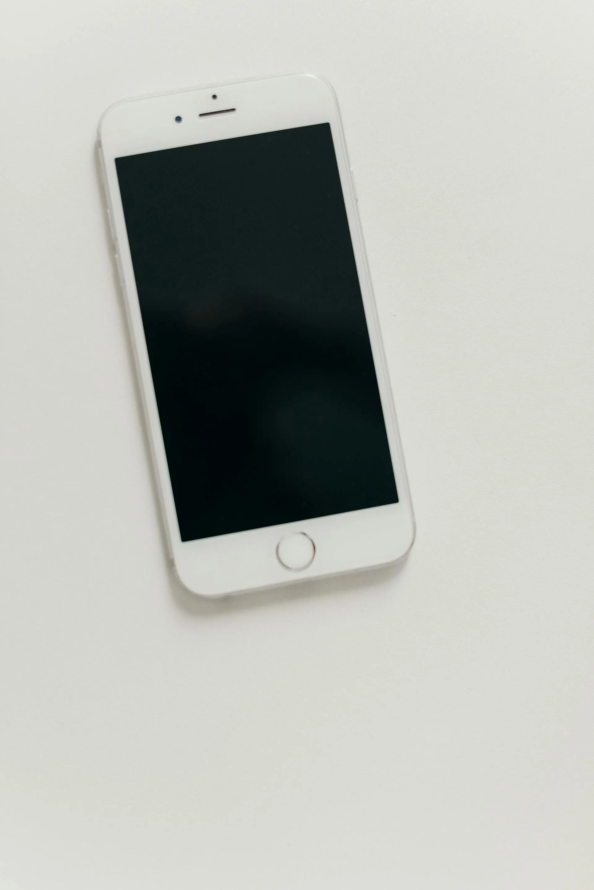 Weißes Smartphone mit schwarzem Bildschirm liegt auf einer weißen Oberfläche.