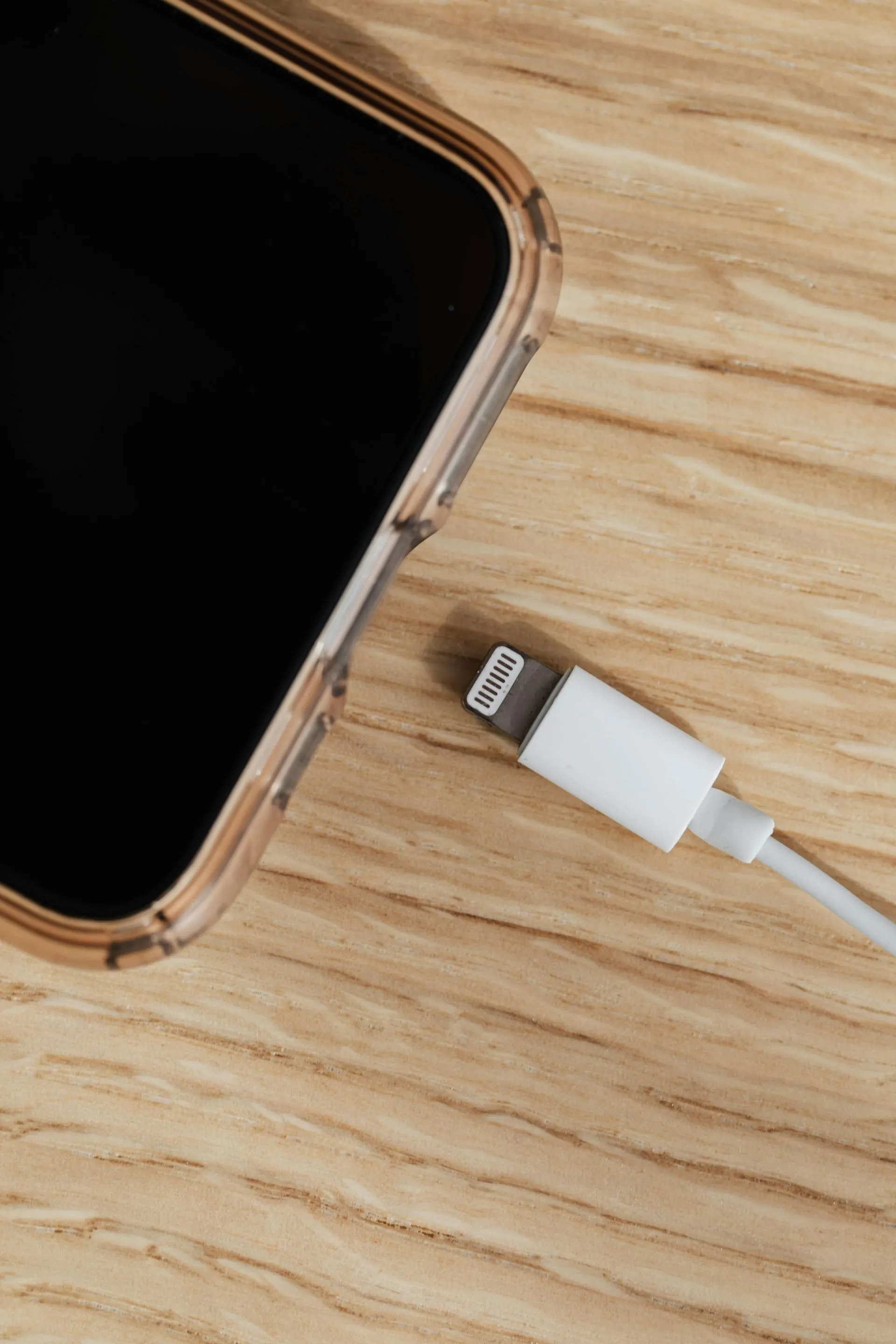 Smartphone mit weißem Ladekabel auf einer Holzoberfläche.