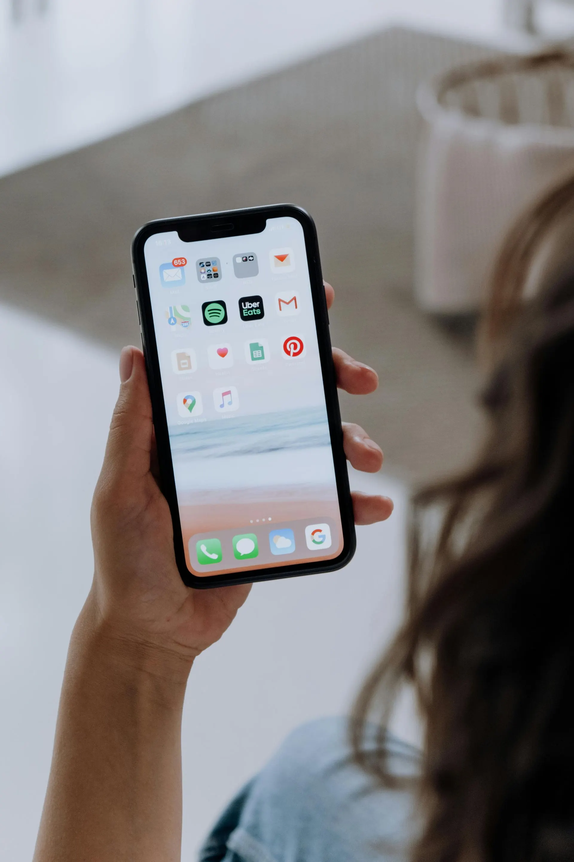 Eine Person hält ein Smartphone in der Hand, auf dem Apps angezeigt werden, und nutzt es möglicherweise in Innenräumen.