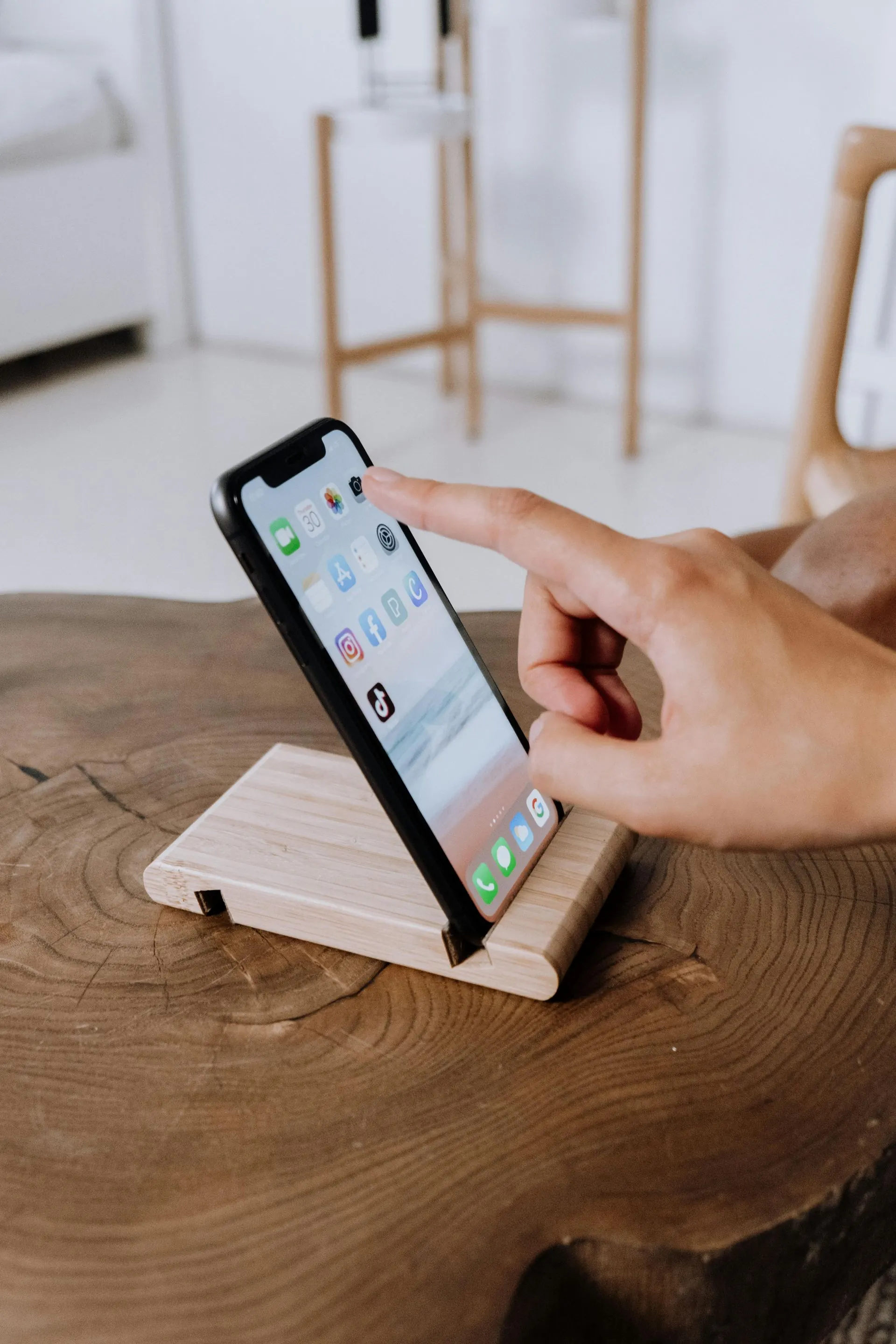 Eine Hand berührt ein Telefon auf einem Holzständer, der auf einem dunklen Holztisch steht.
