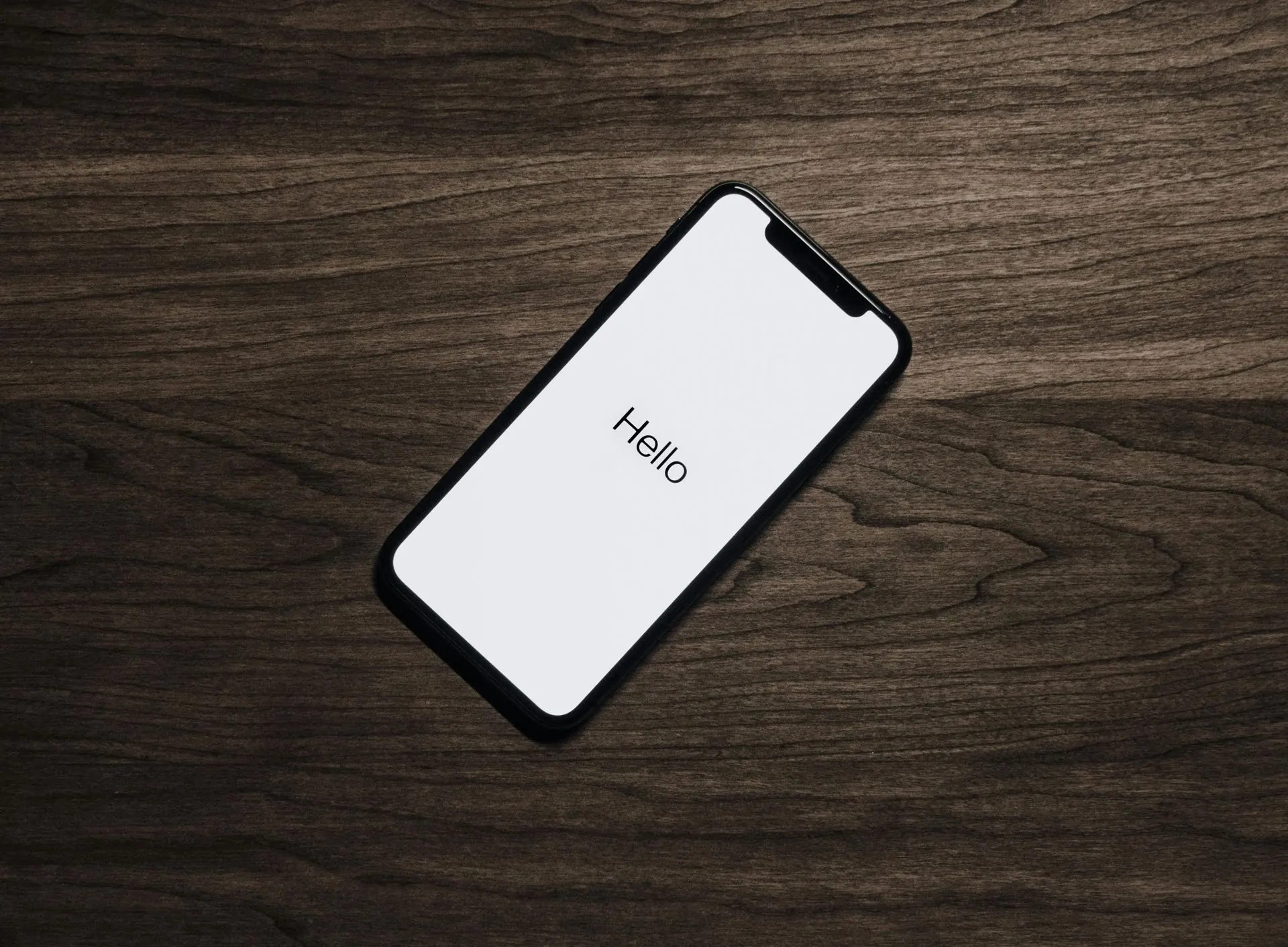 Ein Smartphone auf einer dunklen Holzoberfläche, auf dessen Bildschirm das Wort „Hallo“ angezeigt wird.