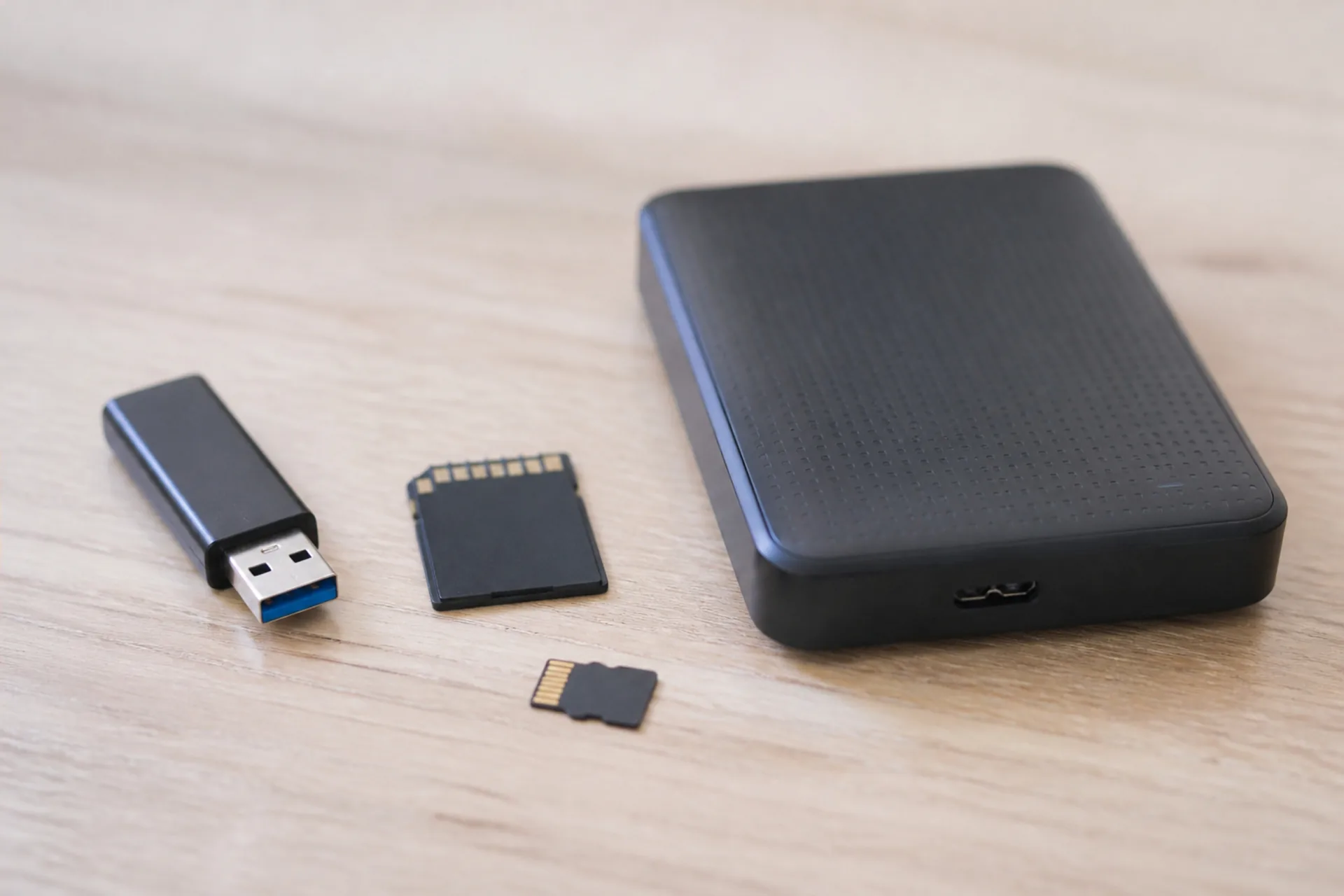 USB-Stick, SD-Karte, microSD-Karte und externe Festplatte auf einem hellen Holztisch.