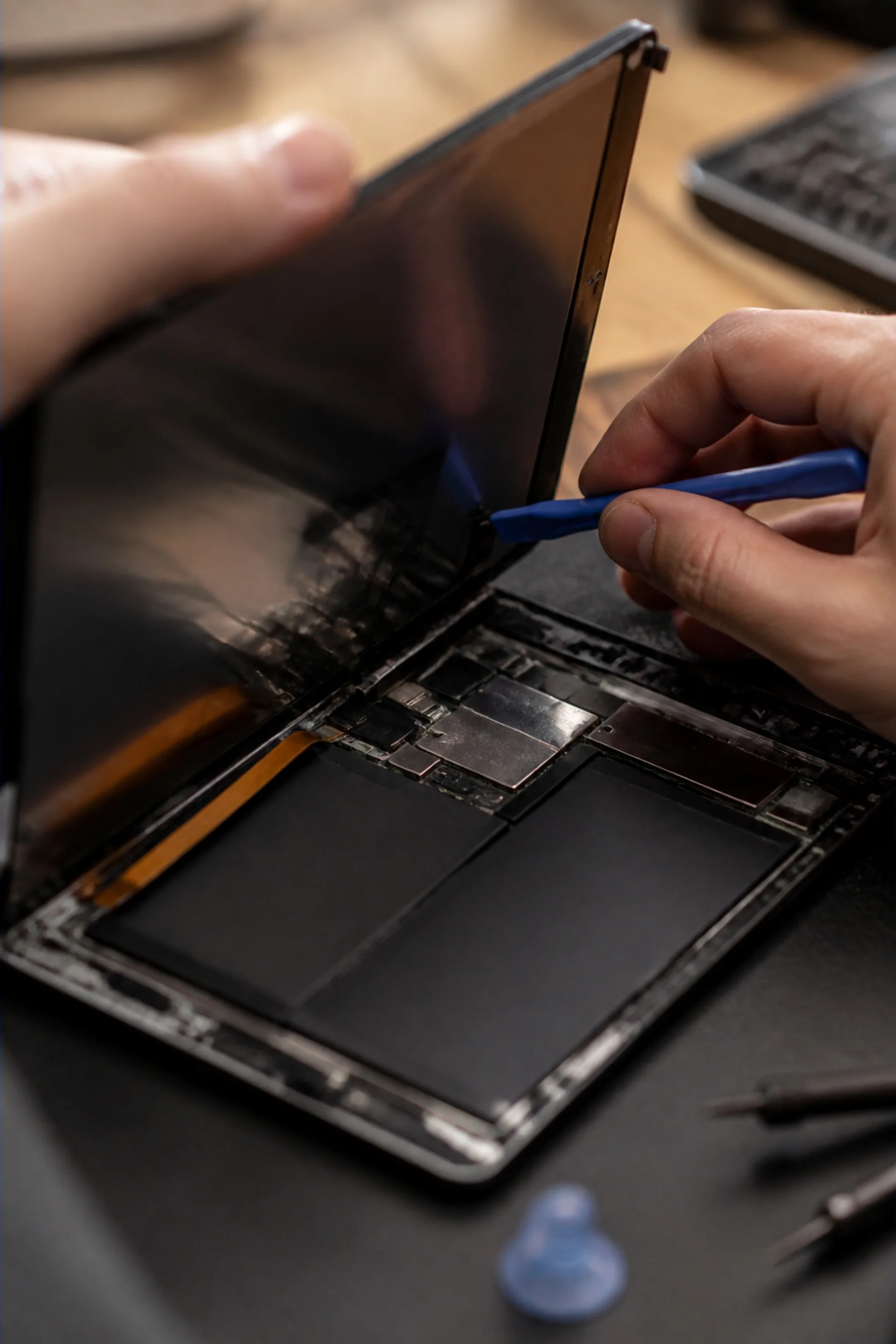 Hände heben mit einem Kunststoffwerkzeug das Display eines geöffneten Tablets an, Akku und Platine sind sichtbar.